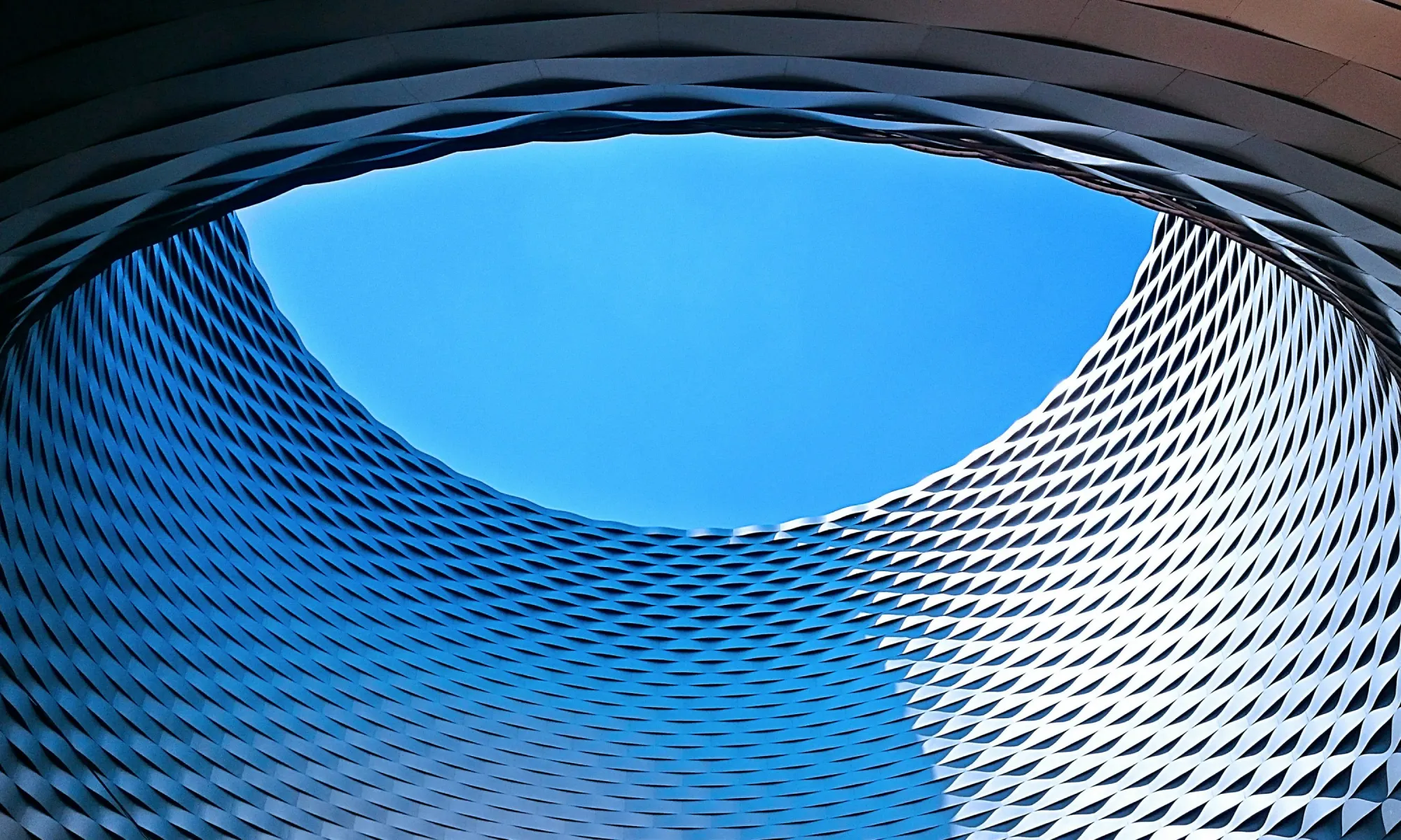 Futuristic building with curved metal panels and a circular opening revealing blue sky