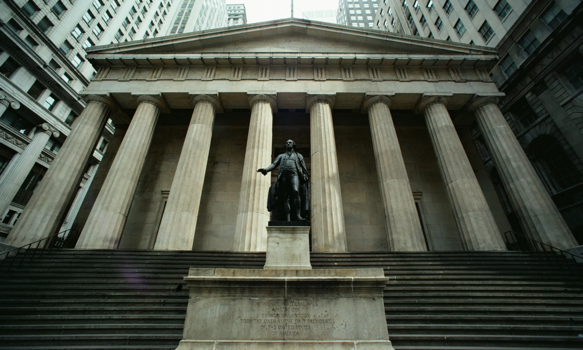 A photo of a neoclassical financial building with large stone columns and a statue of George Washington in front. Represents the traditional financial system and conventional real estate investment vehicles like REITs.