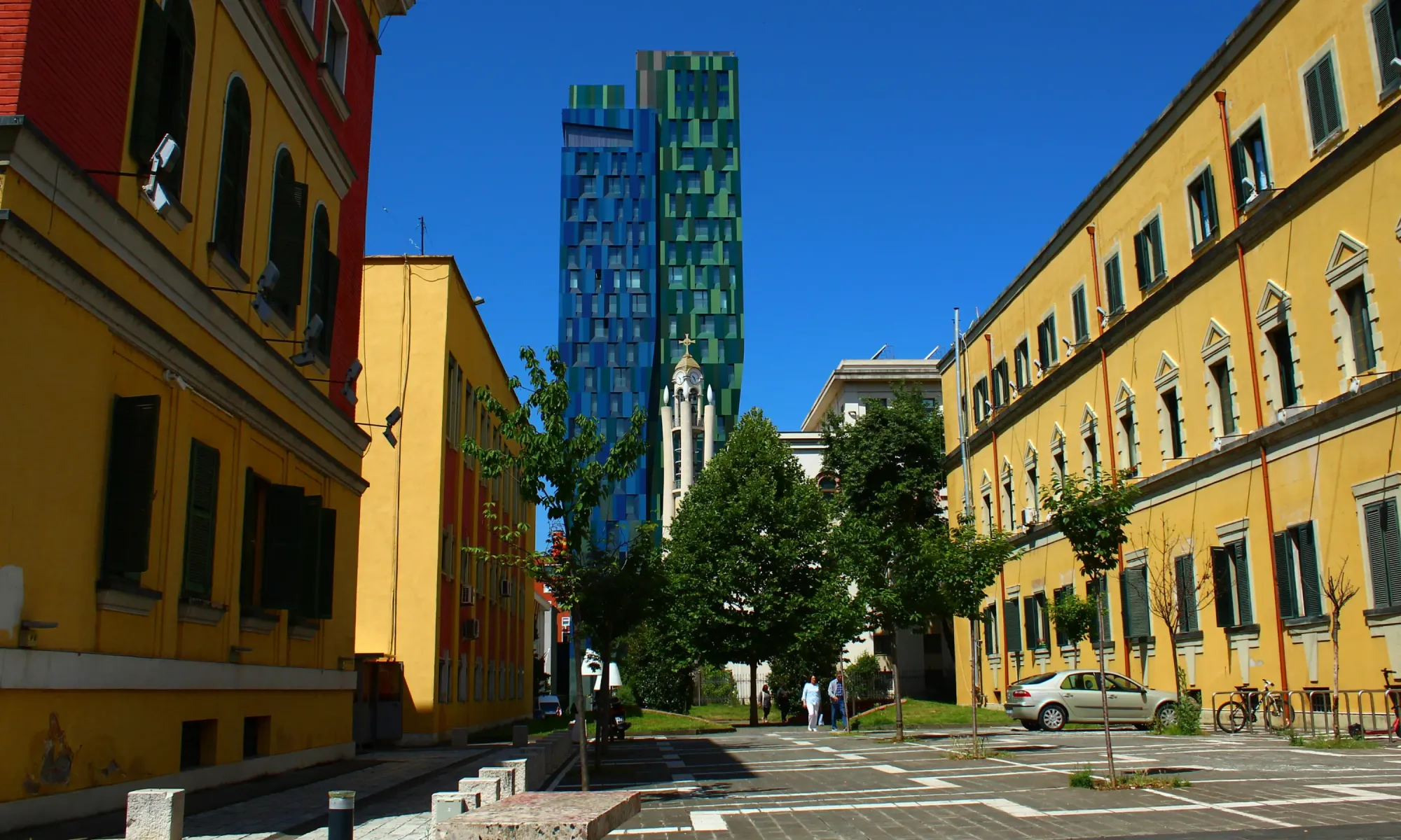 Brightly painted yellow buildings in Tirana with modern blue and green high-rise towers in the background.