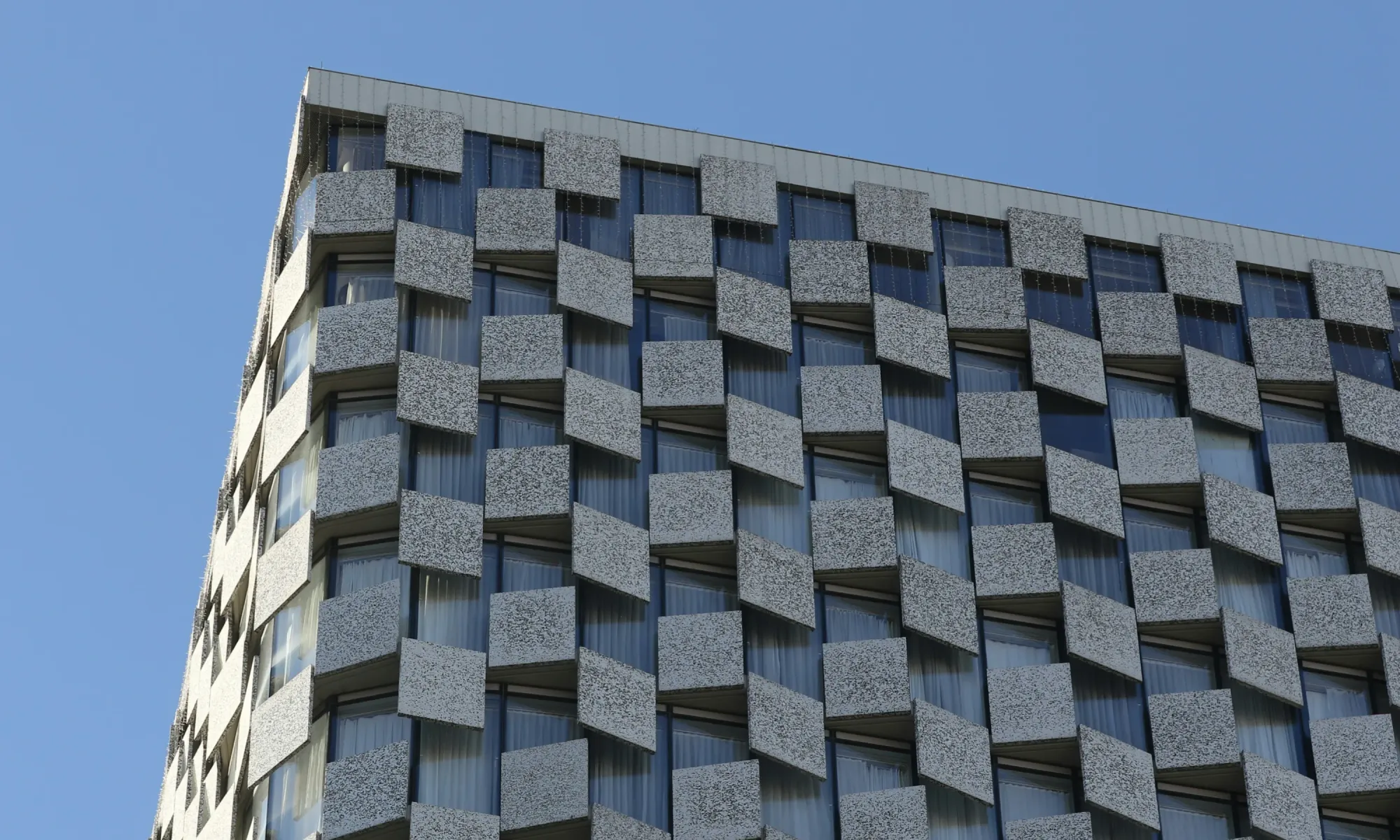 Close-up view of a modern building facade with repeating geometric concrete and glass window patterns.