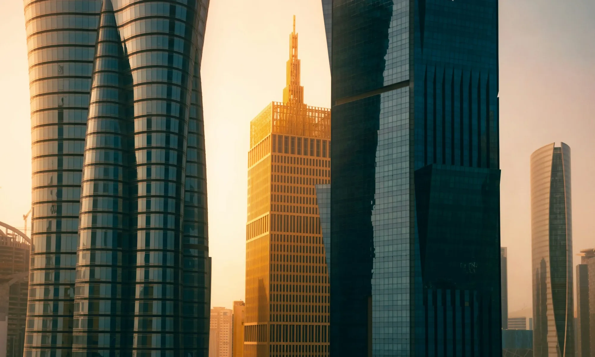 Golden sunset illuminating a slender, gold-toned skyscraper framed by two glass, curving towers and other modern high-rises in the background.