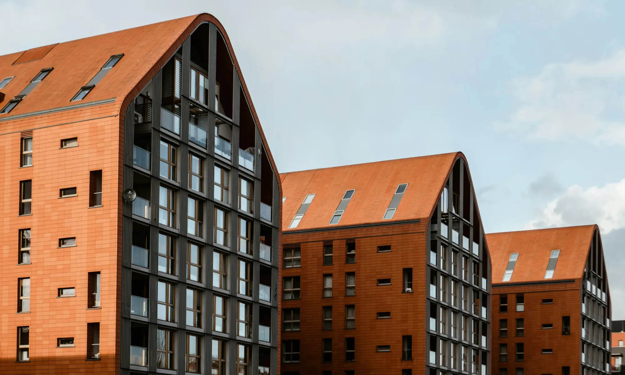 Contemporary residential buildings with sloped red roofs and large windows, designed in a modern architectural style.