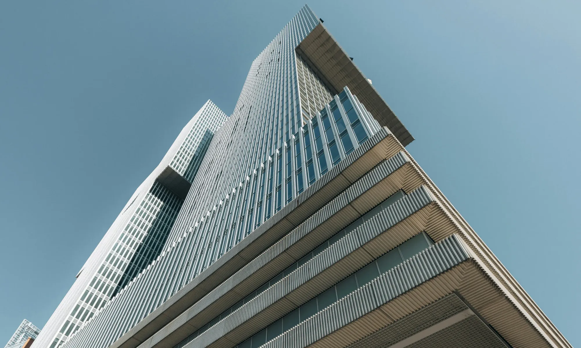 Low-angle view of a sleek modern skyscraper with glass and steel facade under a clear blue sky.